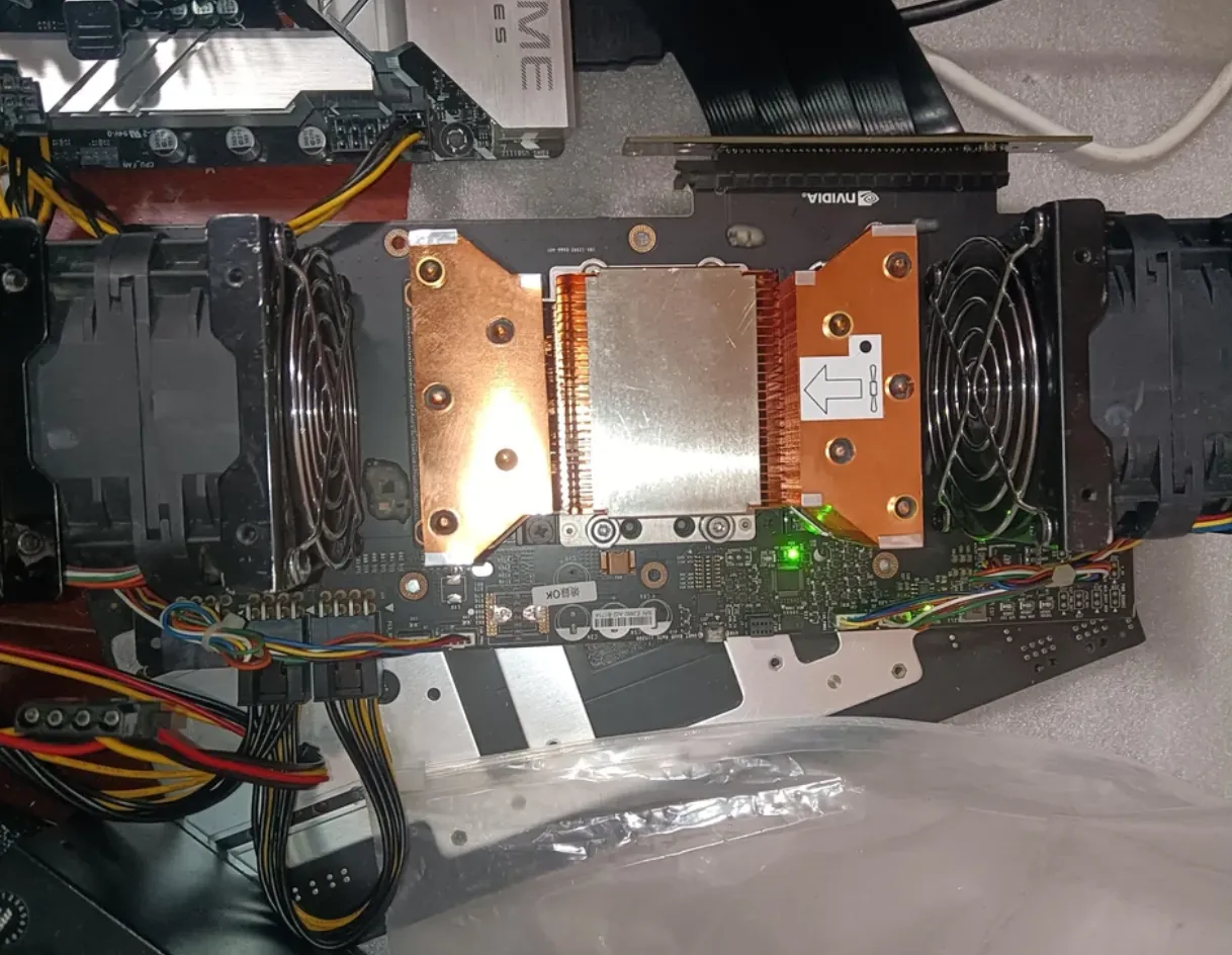 Close-up of an NVIDIA V100 SXM2 module under a copper heatsink, mounted on an SXM2-to-PCIe adapter board between two blower fans, next to an ASUS motherboard and PSU cables.